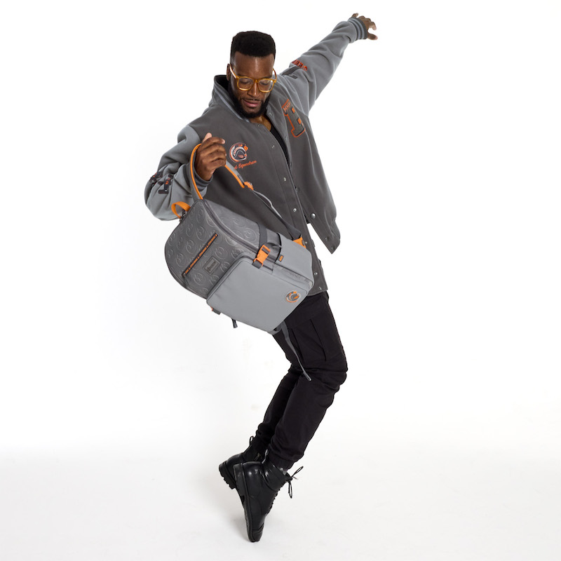 Man with beard and glasses wearing the Loungefly COLLECTIV Star Wars Rebel Alliance VRSITY Jacket and holding the Loungefly COLLECTIV Star Wars Rebel Alliance The MULTI-TASKR Full-Size Backpack in one hand and standing on the toes of his black shoes with his free arm up behind him