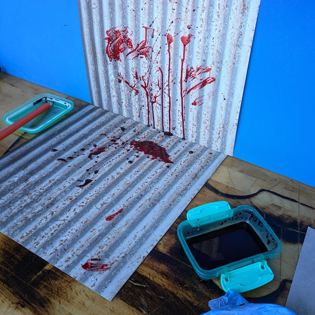 Photography set of corrugated metal, blood spatters, a tray of "blood," and a blue screen behind the metal space.
