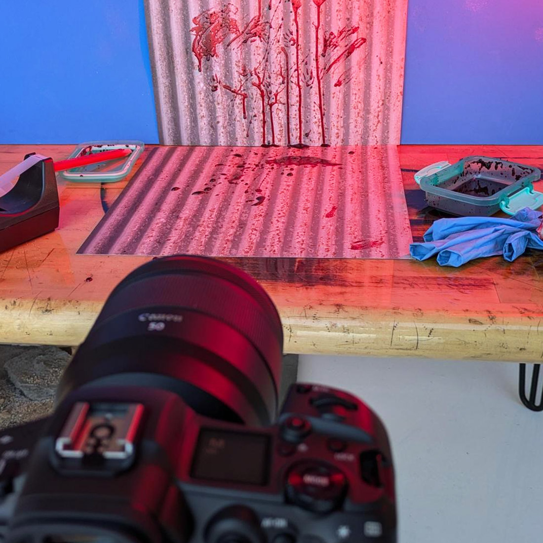 Photography set with blood spatters and corrugated metal and a camera in the foreground with a bit of red light
