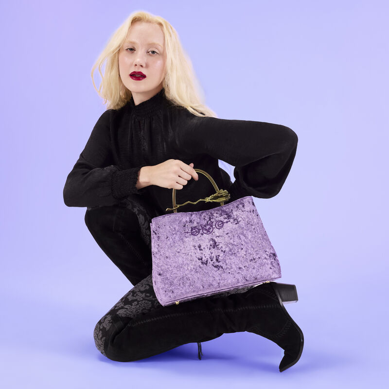 Woman kneeling down in an all-black outfit holding the Loungefly Hocus Pocus Velvet Crossbody Bag. 