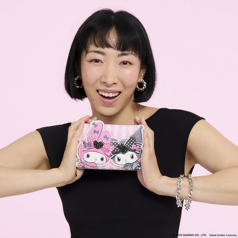 Woman wearing a black top and holding up the Loungefly My Melody and Kuromi zip around wallet. She stands against a light pink background. 