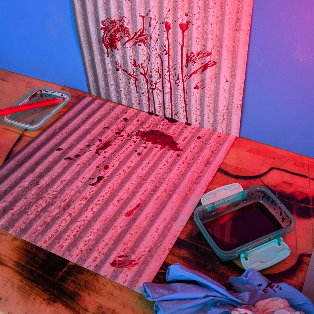 Photography set with the corrugated metal, blood spatters, tray of "blood" and blue screen behind, with a bit of red light